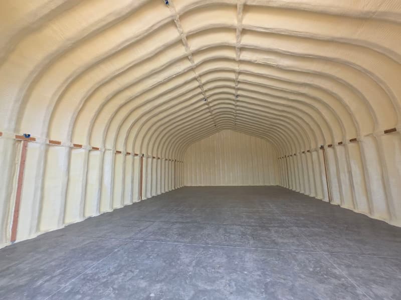 Arched, Quonset-style building with spray foam over the whole curved shell and end wall, concrete floor below