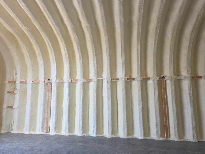 Side wall of an arched, Quonset-style building with foam following the ribbed shell and wood strips fastened across it