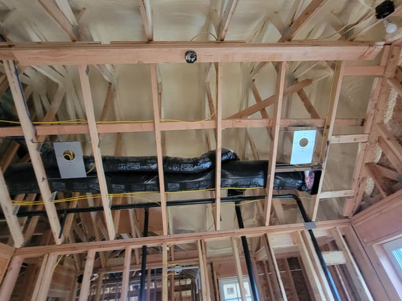 Ceiling joists with spray foam on the deck above and insulated ductwork running between them