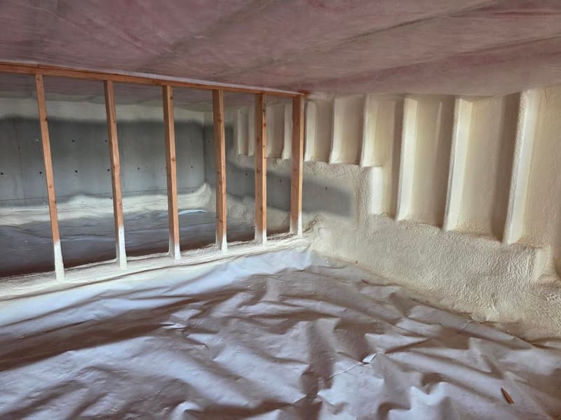 Crawl space with spray foam on the concrete foundation wall and into the rim joist bays, plastic sheeting over the ground