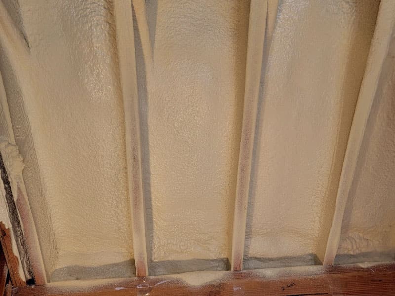 Close-up of cured spray foam filling the rafter bays of a sloped ceiling