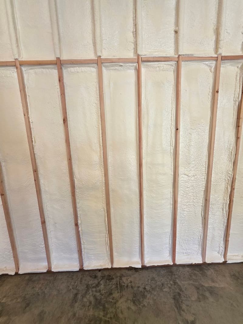 Close view of spray foam filling the bays between wood studs down to a concrete floor
