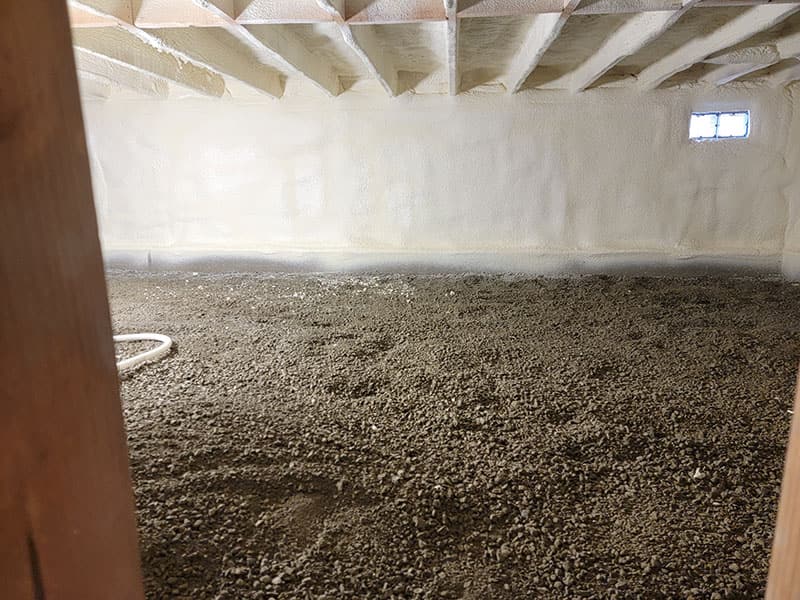 Building shell with spray foam covering the walls and ceiling and a gravel floor not yet poured
