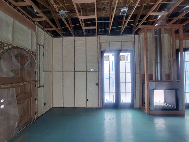 Room with spray-foamed walls and open ceiling framing, French doors and a fireplace insert