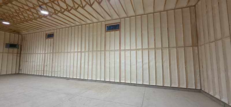 Long garage wall with spray foam between the studs from floor to ceiling, two small windows and foamed roof framing above
