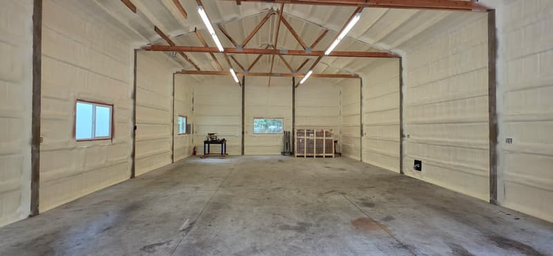 Wide view of a large building with spray foam covering every wall and the roof, open wood trusses and a concrete floor