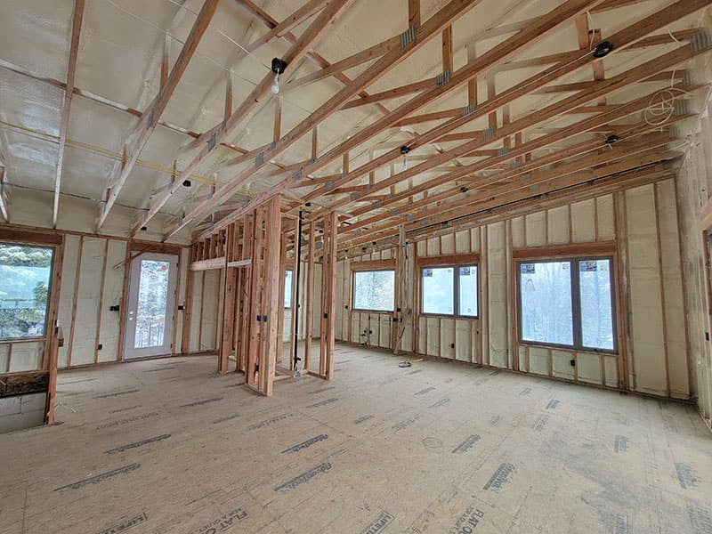 Long open room with spray foam on the exterior walls and ceiling, several window openings and interior framing still exposed