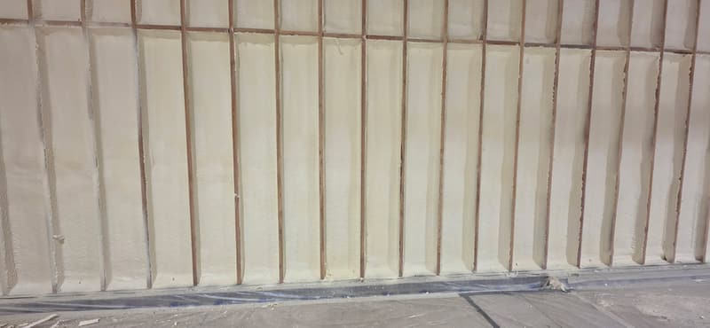Long framed wall with spray foam filling every bay between the studs, plastic sheeting protecting the floor