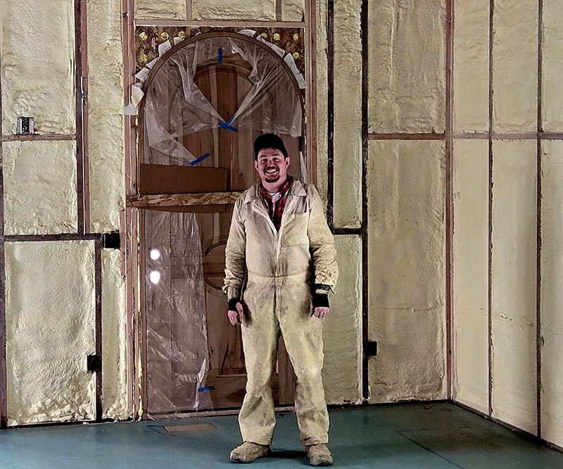 Nick Bond, owner of Empire Insulation, in a white protective suit standing in a room freshly sprayed with foam