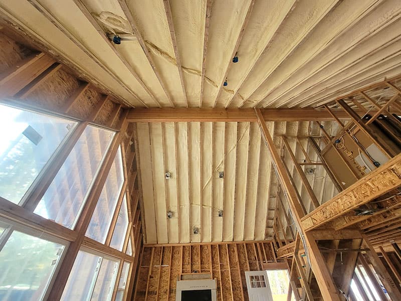 Peaked roof with spray foam between the rafters above a gable wall of windows