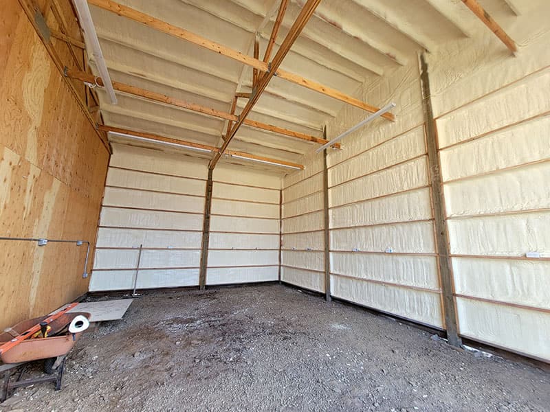 Pole barn interior with spray foam on the walls and roof between the wood girts and purlins, dirt floor