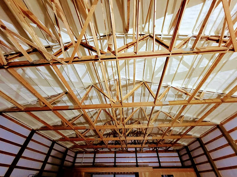 Pole building roof trusses seen from below, with spray foam applied to the roof between the purlins