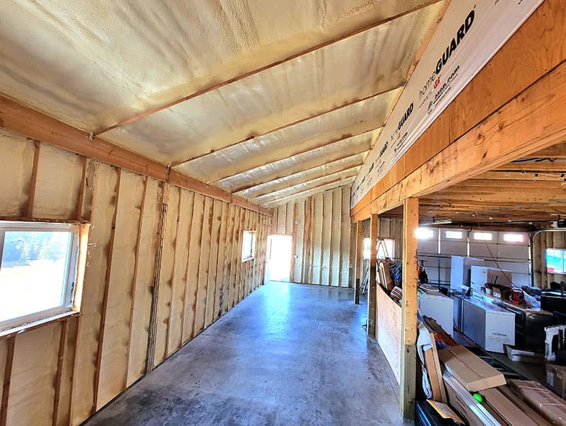 Long shop space with spray foam on the walls and roof, concrete floor, and equipment stored along one side