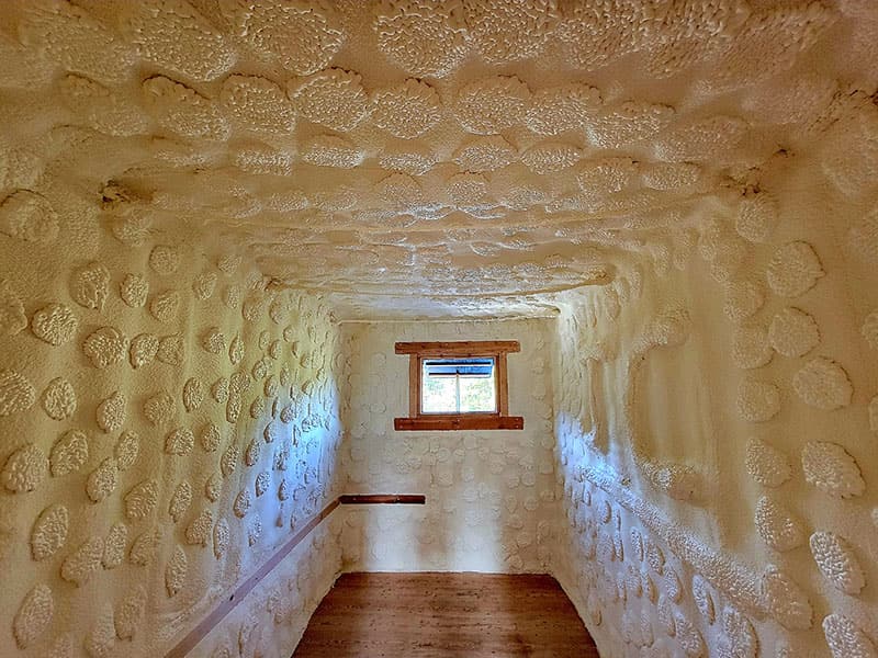 Small room with spray foam covering the walls and ceiling completely, one window and a wood floor