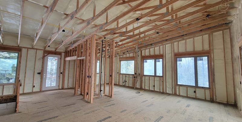 Wide view of a framed home interior with spray foam on every exterior wall between the studs and around the window openings