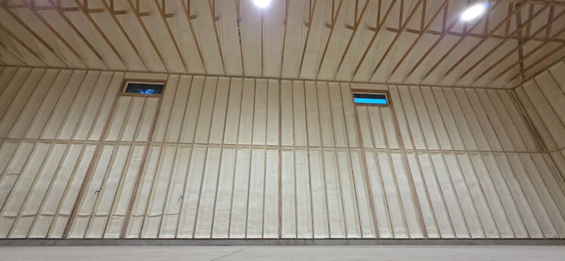 Tall framed wall with spray foam between the studs, two small high windows and foam between the roof framing above
