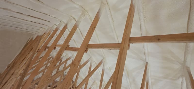 Wood roof trusses with spray foam covering the underside of the roof from the peak down the slope