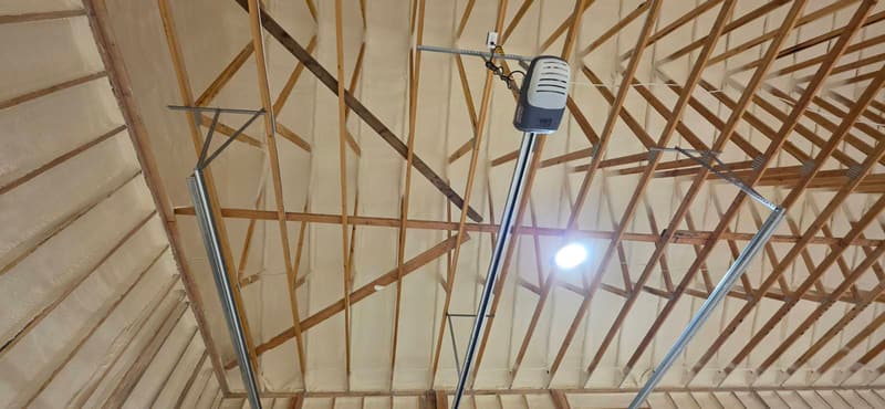 Wood roof trusses below a foam-covered roof, with a garage door opener and its rails mounted among them