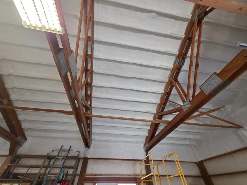 Wood trusses with metal gusset plates below a roof sprayed with foam between the purlins, scaffolding underneath