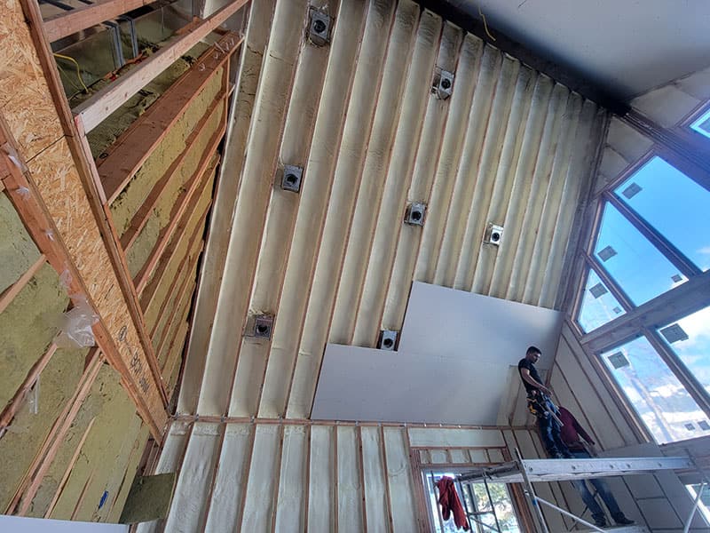 Looking up a two-story stairwell with spray foam in the wall cavities and the ceiling, scaffolding and a ladder below